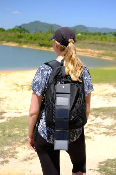 Chargeur solaire Photon de Sunslice – mise en situation : déplié sur un sac à dos porté par une personne face à un lac