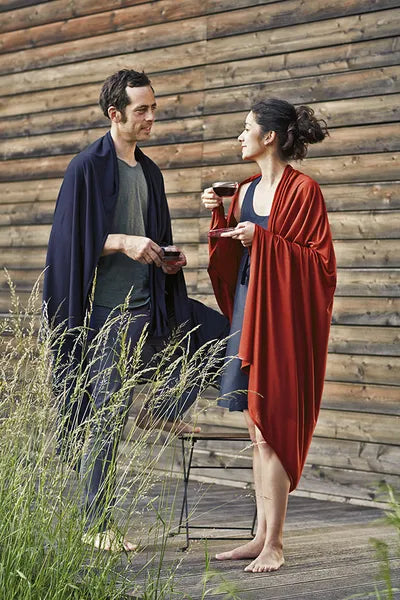 Couverture de voyage en laine et soie – mise en situation : la couverture bleu marine est portée par un homme debout, la terracotta par une femme debout.