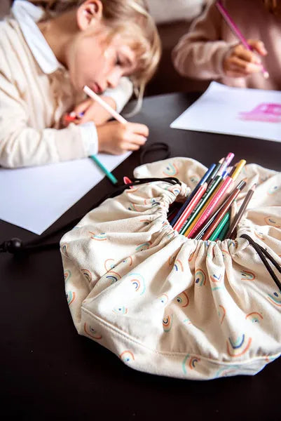 Mini sac de rangement et tapis de jeux motif arc-en-ciel de Playandgo - vue du sac ouvert avec des crayons et des enfants qui dessinent en arrière plan