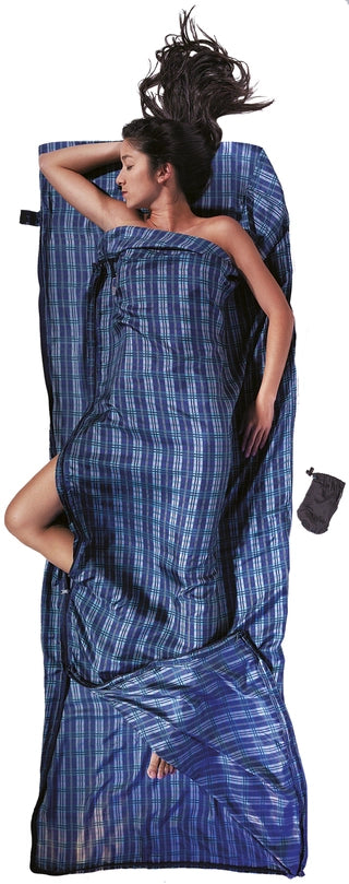 Housse de lit zippée en soie de Cocoon - carreaux bleu en soie - Mise en situation : une personne dort dans la housse de lit avec la pochette posée à côté, utilisée en version simple