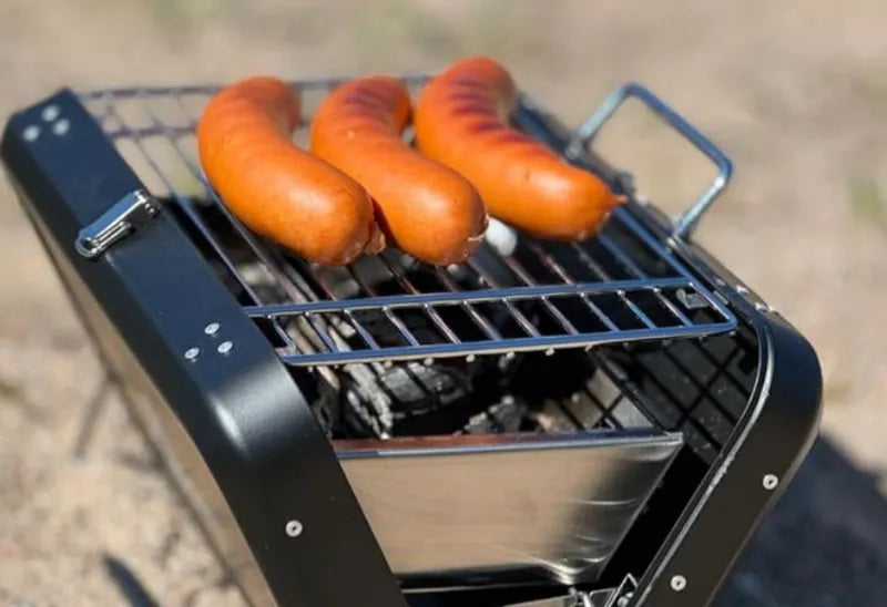Barbecue à charbon pliable portatif de kikirikit noir - gros plan sur la grille de cuisson avec saucisses qui cuisent