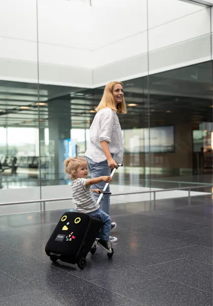 Valise trolley avec siège enfant intégré Micromobility – mise en situation : une femme tire la valise avec une petite fille assise dessus dans un aéroport
