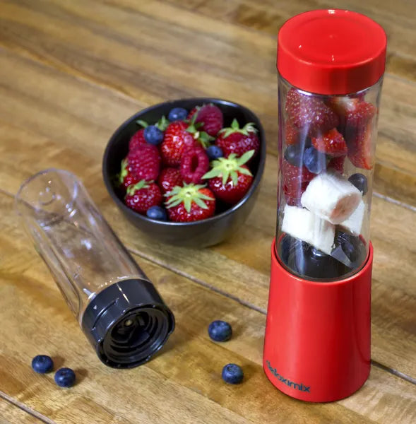Mini Blender Detoximix rouge – Mise en situation avec des fruits entiers dans la bouteille de 280 ml et une bouteille supplémentaire présentée couchée.