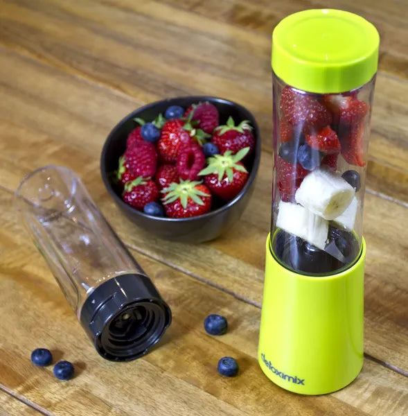 Mini Blender Detoximix vert – Mise en situation avec des fruits entiers dans la bouteille de 280 ml et une bouteille supplémentaire présentée couchée.