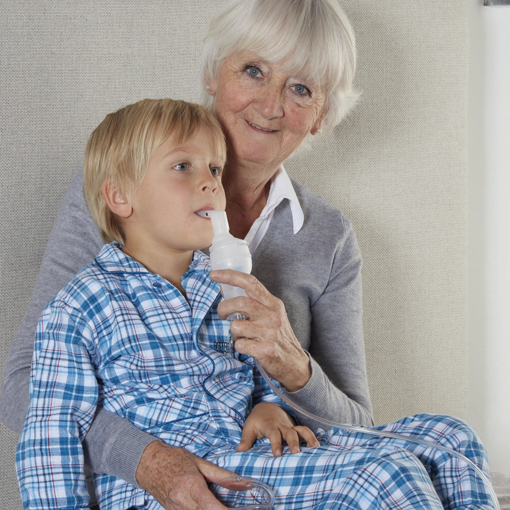Aérosol compact en utilisation par une dame tenant d'une main l'aérosol et de l'autre plaçant l'embout dans la bouche d'un enfant