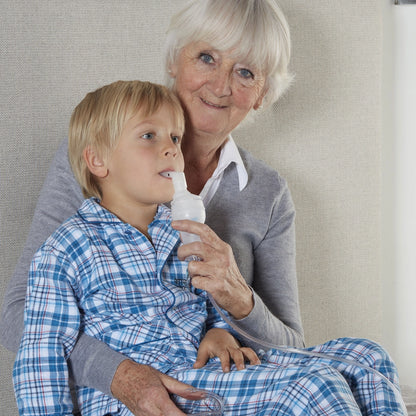 Aérosol compact en utilisation par une dame tenant d'une main l'aérosol et de l'autre plaçant l'embout dans la bouche d'un enfant