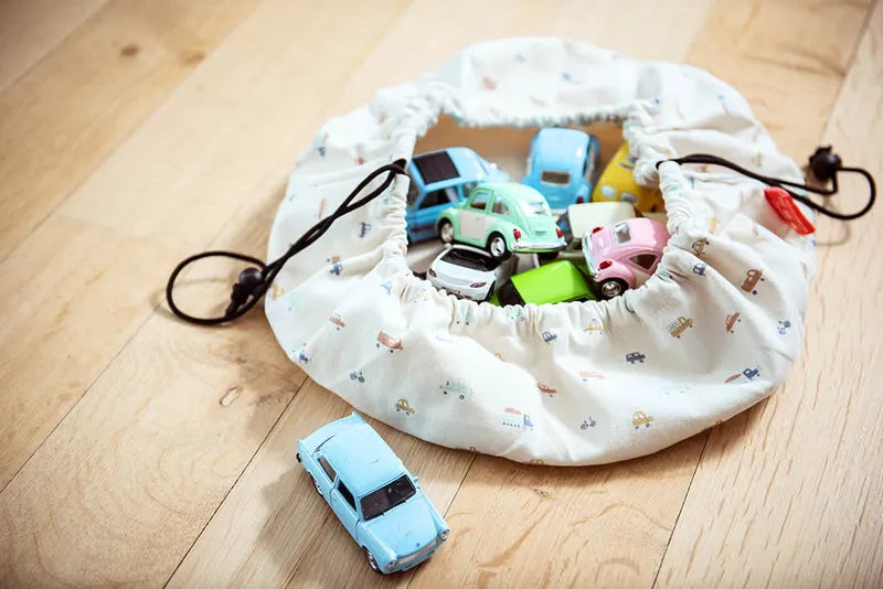 Mini sac de rangement et tapis de jeux motif voitures de Playandgo - vue du sac ouvert avec des voitures à l'intérieur et une voiture bleue à l'extérieur du sac 