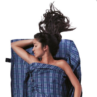Housse de lit zippée en soie de Cocoon - carreaux bleu en soie - Mise en situation : une personne dort dans la housse de lit avec la pochette posée à côté, utilisée en version simple