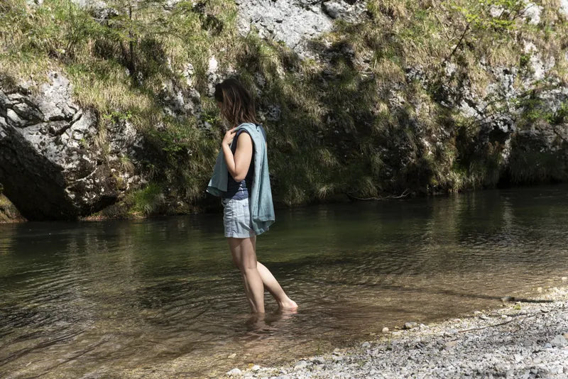 Serviette de voyage ultralégère Cocoon – mise en situation : modèle vert d’eau posé sur l’épaule d’une femme aux pieds dans l’eau.