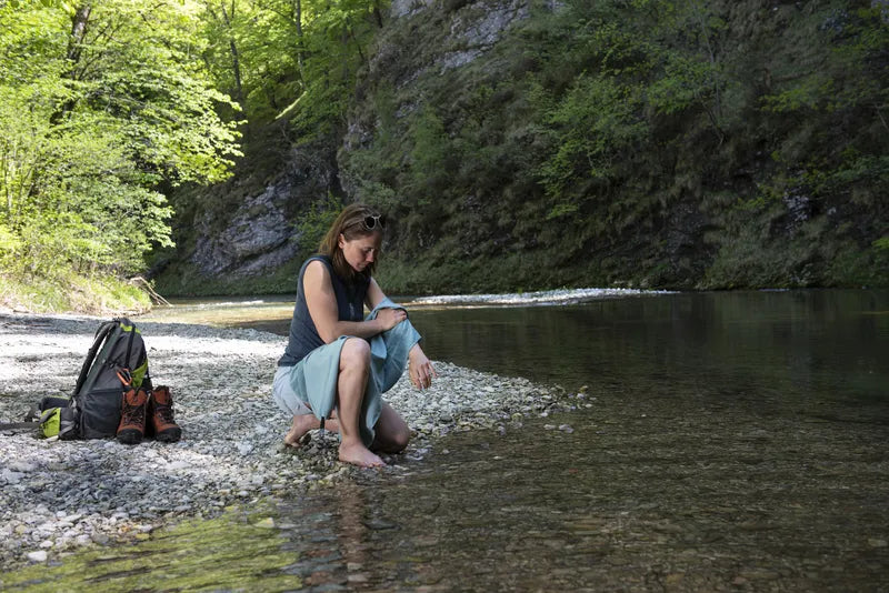 Serviette de voyage ultralégère Cocoon – mise en situation : modèle vert d’eau utilisé au bord d’une étendue d'eau, une femme s’essuie le bras avec.