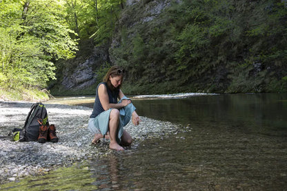 Serviette de voyage ultralégère Cocoon – mise en situation : modèle vert d’eau utilisé au bord d’une étendue d'eau, une femme s’essuie le bras avec.