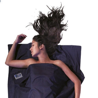 Housse de lit adulte en coton Egyptien de Cocoon - Marine - Housse de lit adulte en coton et soie Cocoon – bleu – mise en situation : une personne dort dans le drap, la pochette placée juste à côté.