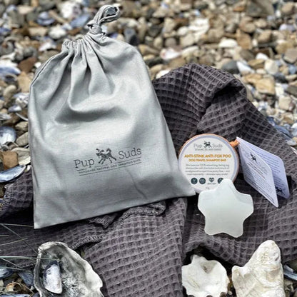 Savon de voyage et serviette de voyage pour chien de Pupsuds - mise en situation sur une plage de galet du savon et de la serviette